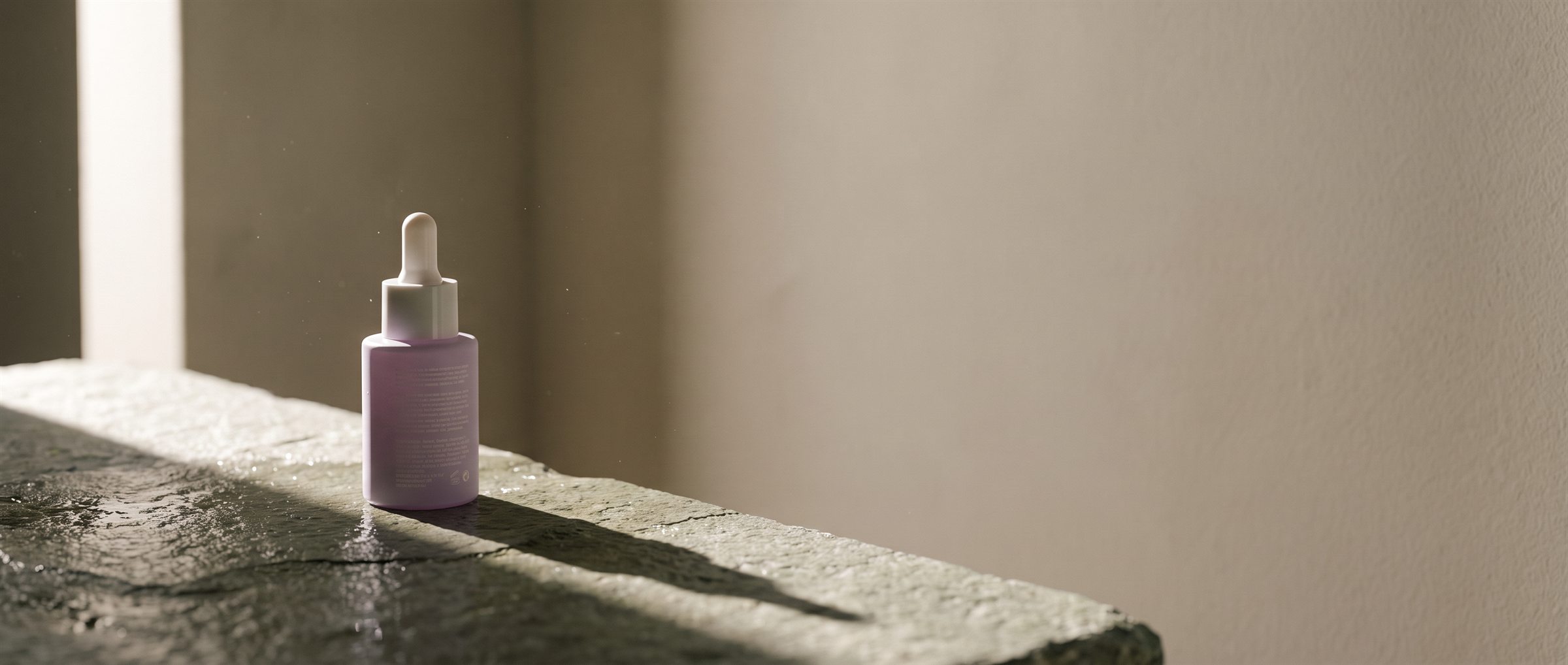 Sérum reparador Musu Radiance sobre piedra húmeda con luz rasante
